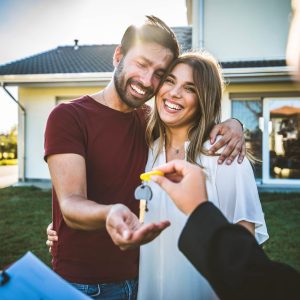 Happy millennial couple receiving keys from realtor, purchasing real estate - Family meeting with real estate agent - New house and real estate concept